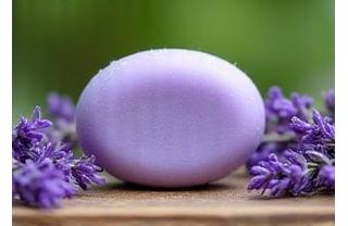 Sabonete Artesanal de Lavanda: barra arredondada roxa em superfície de madeira com flores de lavanda frescas em volta